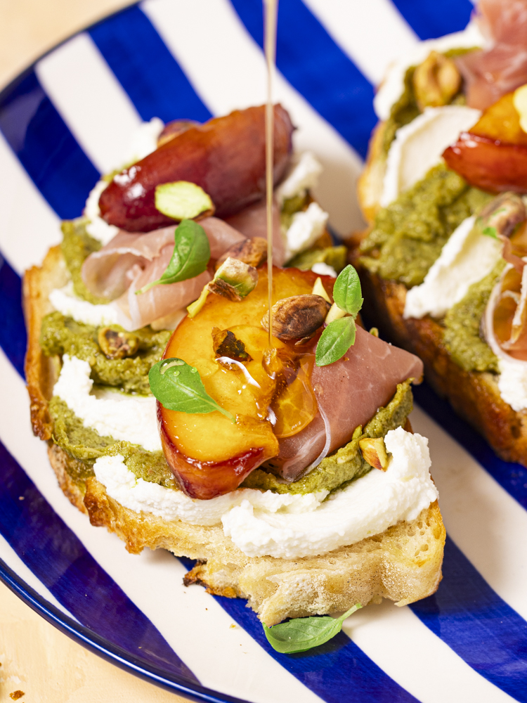 Tartine de pain de campagne garni de pesto, de pêches, de ricotta, de fromages frais, d'un filet de miel, de jambon cru et de basilic